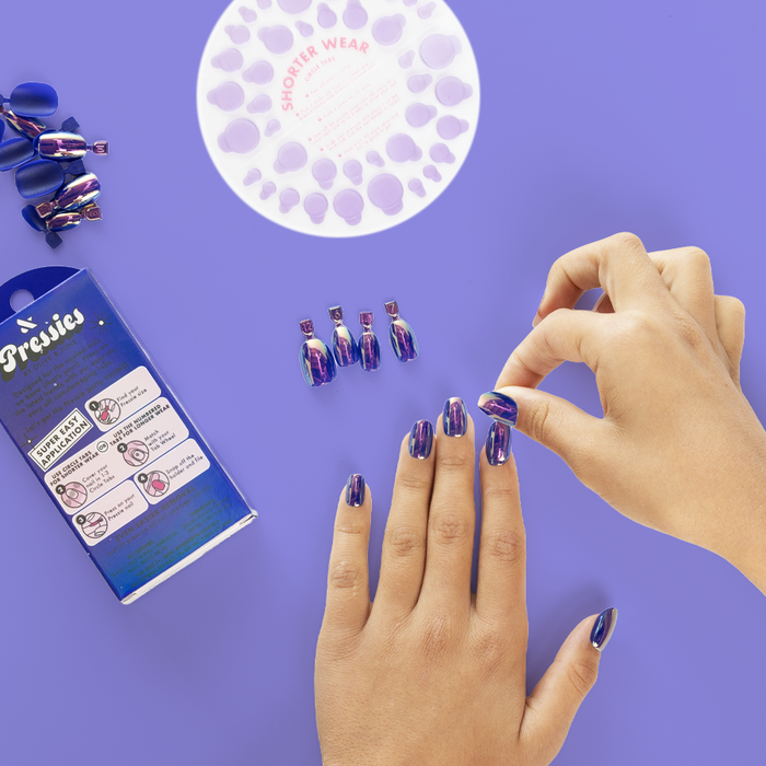 Blue Chrome Magic - Pressies | Short Medium | Round showing hand applying deep blue chrome press on nails on purple surface