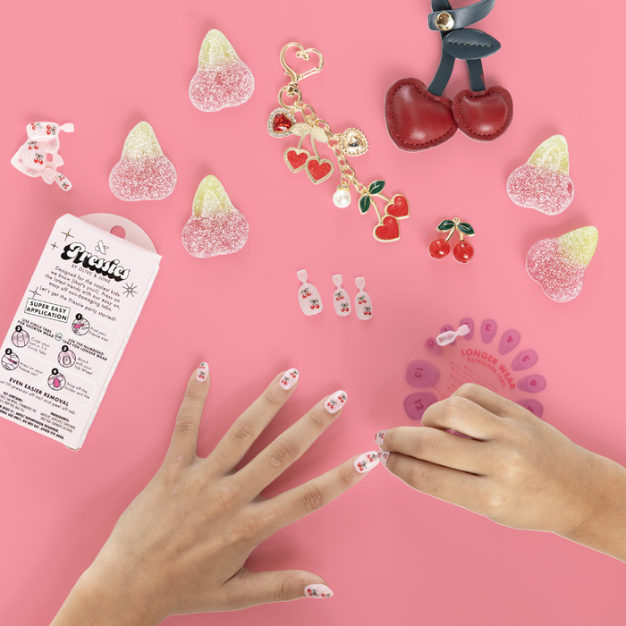 Cherry Whirl - Pressies | Short Medium | Round showing kid applying pink press on nails with cherry designs on pink background