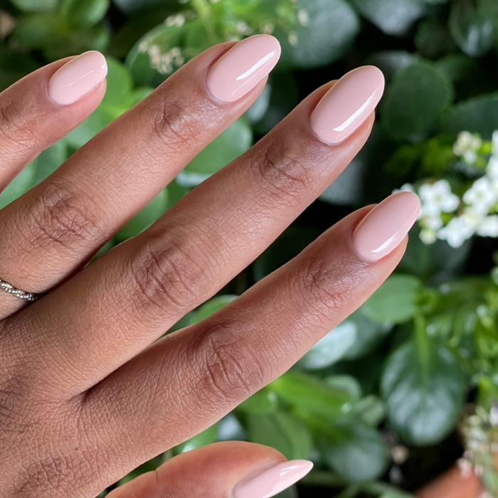 Hand with oval nails painted in KAG - Gel neutral peachy pink gel polish against green leafy background