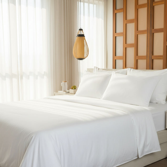 Neatly made bed with white bedding in a bright bedroom with wooden headboard and light fixture.