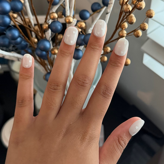 Velvet Pearly Hearts - Tab Press On | Extra Short | Round false nails with white heart design on pearly velvet base shown on hand