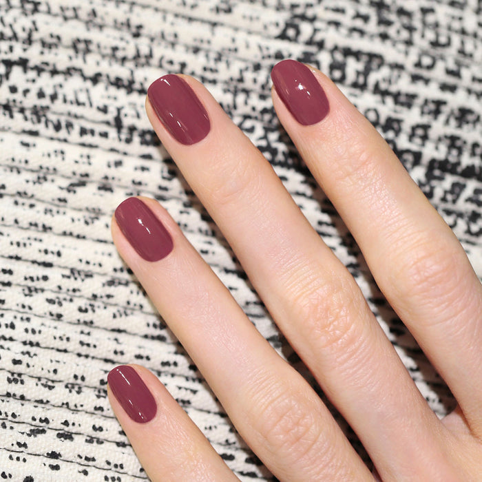 A hand with neatly manicured nails painted in Manucurist's Victoria Plum nail polish rests on a textured black and white patterned surface.