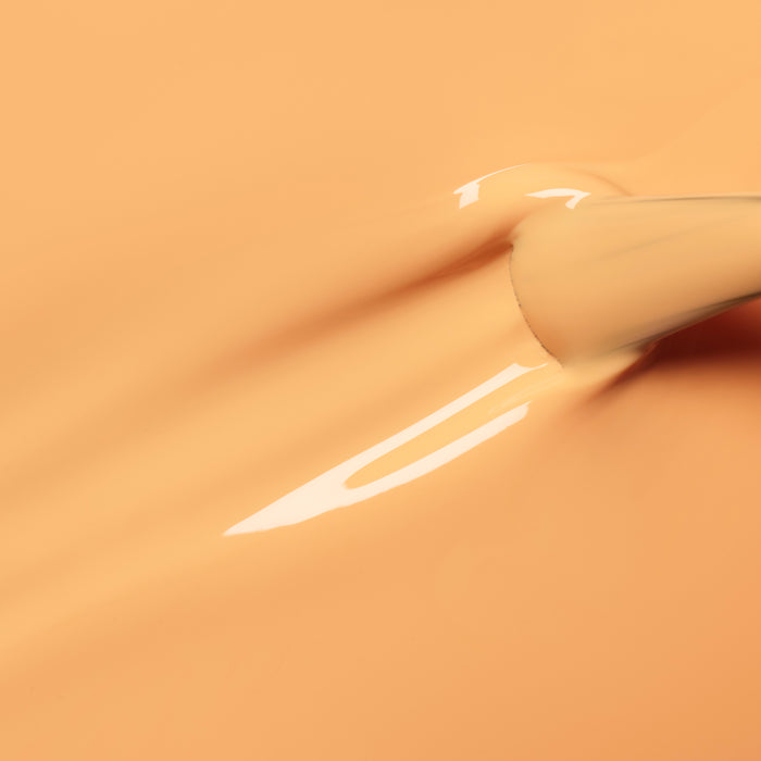 A close-up of a Manucurist Abricot brush spreading creamy pastel orange nail polish, creating smooth, glossy streaks on a matching background.