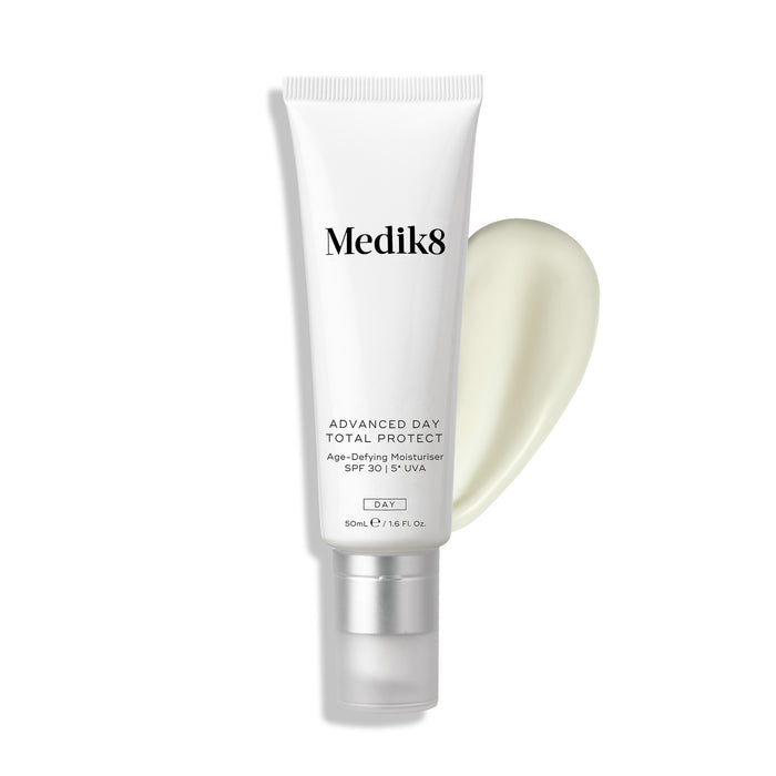 Medik8 Advanced Day Total Protect tube stands against a clean white background with a large, creamy white moisturiser smear. Text identifies the product as an Age-Defying Moisturiser with SPF 30 and 5* UVA protection in a 50mL size.