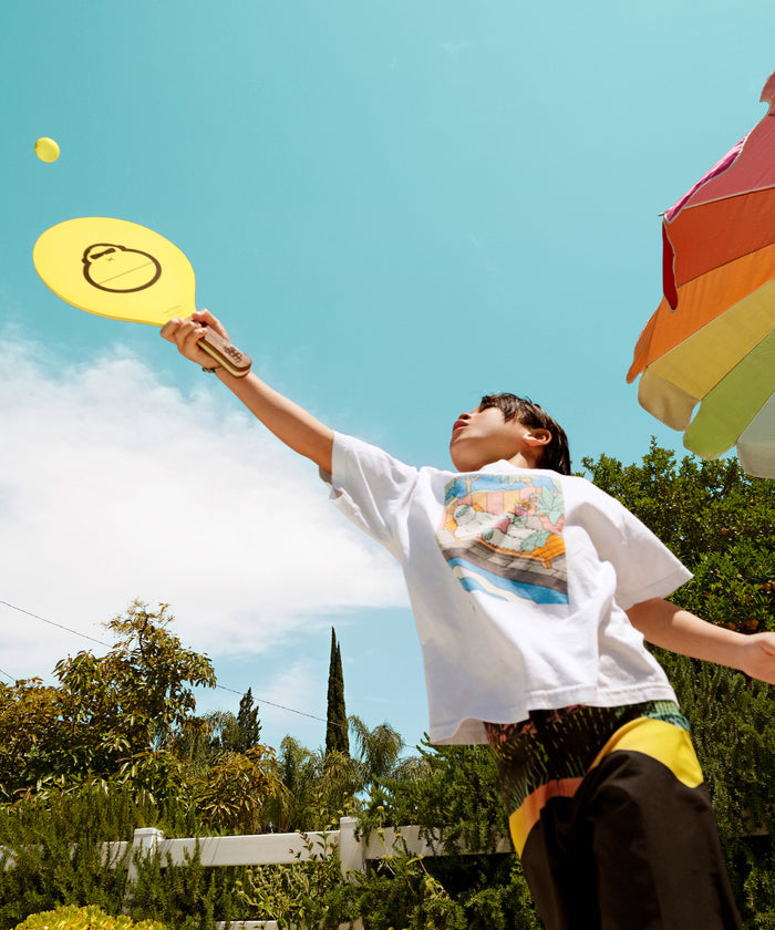Child playing outdoors hitting a ball with a yellow paddle from the Beach Paddleball Set by Sun Bum