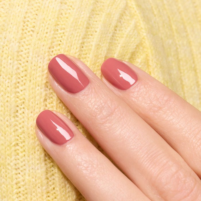 A close-up of a hand with neatly manicured nails painted in Manucurist's glossy Bois de Rose gel polish, resting on yellow knitted fabric.
