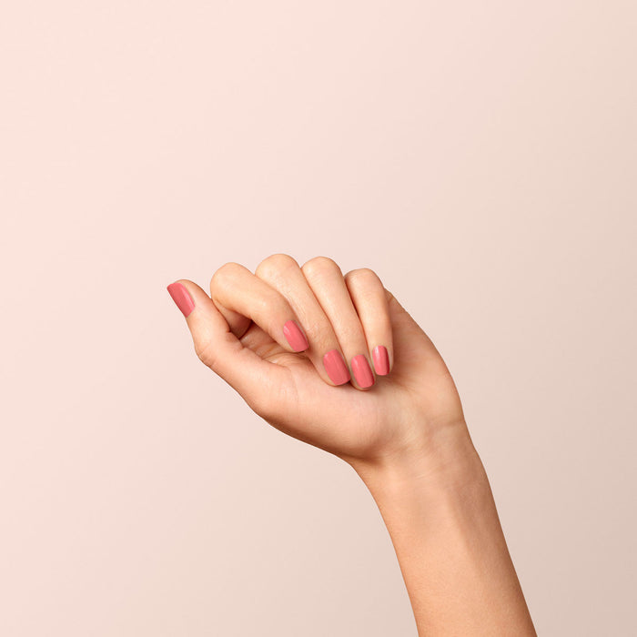 A hand with neatly manicured nails painted in Manucurist's Bois de Rose, a delicate dusty pink gel polish, is held up against a plain light beige background.