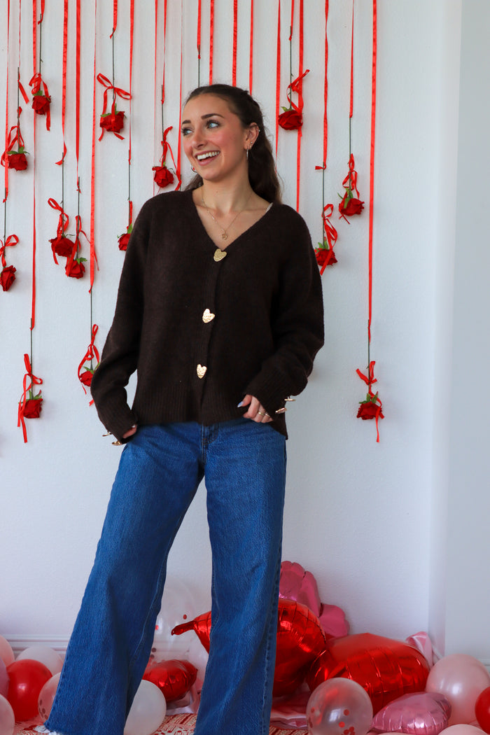 Woman in a black cardigan and blue jeans standing in front of a decorative wall with red ribbons and balloons.