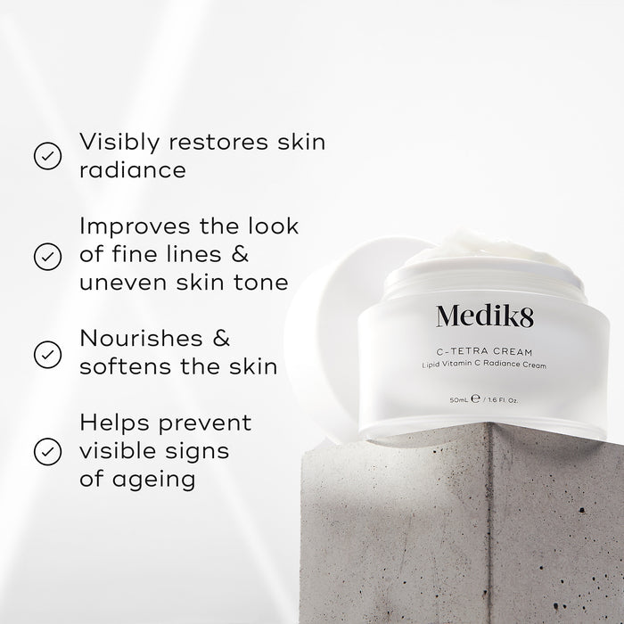 Medik8 C-Tetra Cream jar displayed on a grey stone block against a white background with soft light rays. The image features four check-marked claims: Visibly restores skin radiance, Improves the look of fine lines & uneven skin tone, Nourishes & softens the skin and Helps prevent visible signs of ageing