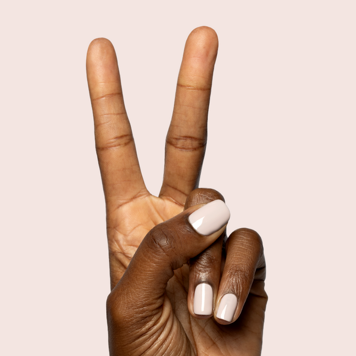 Hand with short nails painted in creamy neutral CDJ - Gel polish by Olive and June against soft beige background