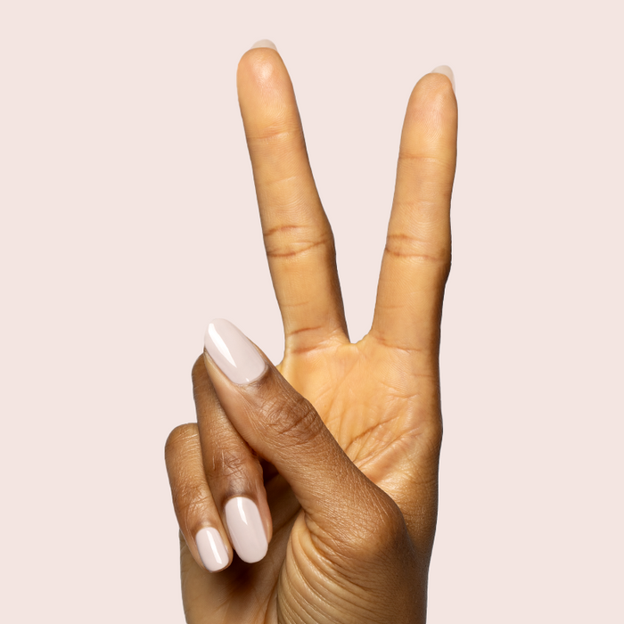 Hand with neutral creamy nails painted in CDJ - Gel polish by Olive and June against soft light background