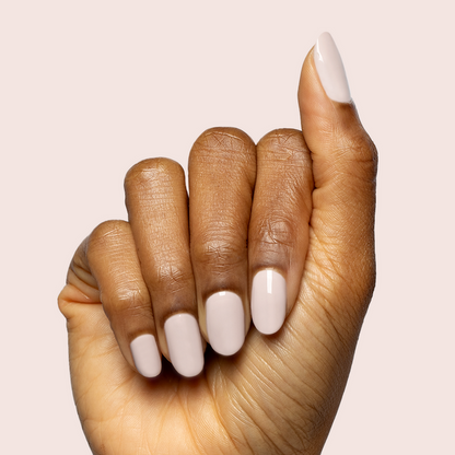 Hand with medium-length nails painted in CDJ - Gel creamy neutral polish on warm skin tone with soft light background
