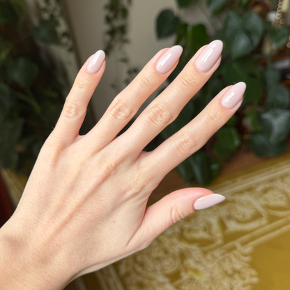 Hand with long almond-shaped nails painted in CDJ - Gel creamy neutral gel polish against blurred indoor background