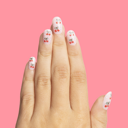 Cherry Whirl - Pressies | Short Medium | Round showing pastel pink press on nails with cherry designs on hand against pink background