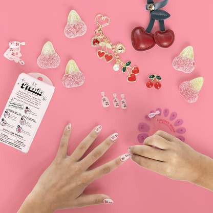 Cherry Whirl - Pressies | Short Medium | Round showing kid applying pink press on nails with cherry designs on pink background