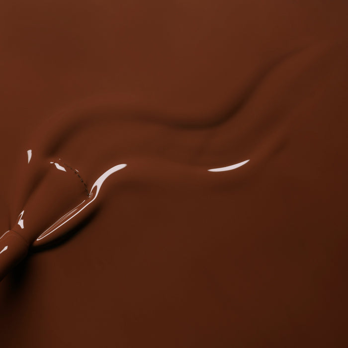 Close-up of smooth, melted chocolate in a warm brown hue being swirled, forming glossy waves that mirror the rich Chestnut shade of Manucurist's Green™ nail polish.