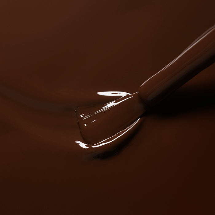 A close-up of a brush applying Manucurist's Green™ nail polish in Clove, a glossy chocolate brown shade, onto a smooth surface for a shiny, even finish.