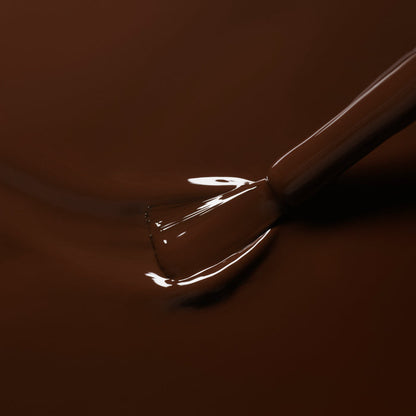 A close-up of a nail polish brush dipping into Manucurist’s Clove, a glossy chocolate brown gel polish, with smooth, shiny liquid coating the bristles.