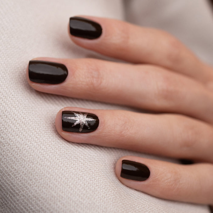 A hand with black painted nails, highlighted by a touch of Manucurist Clove, a rich chocolate brown nail polish.
