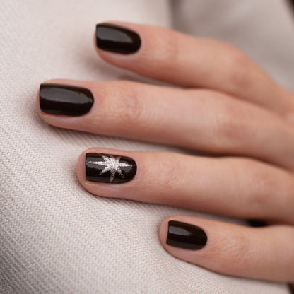 A hand with black painted nails, highlighted by a touch of Manucurist Clove, a rich chocolate brown nail polish.