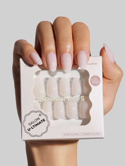 Hand holding a box of white press-on nails with 'Salon Ultimate' branding on a light gray background