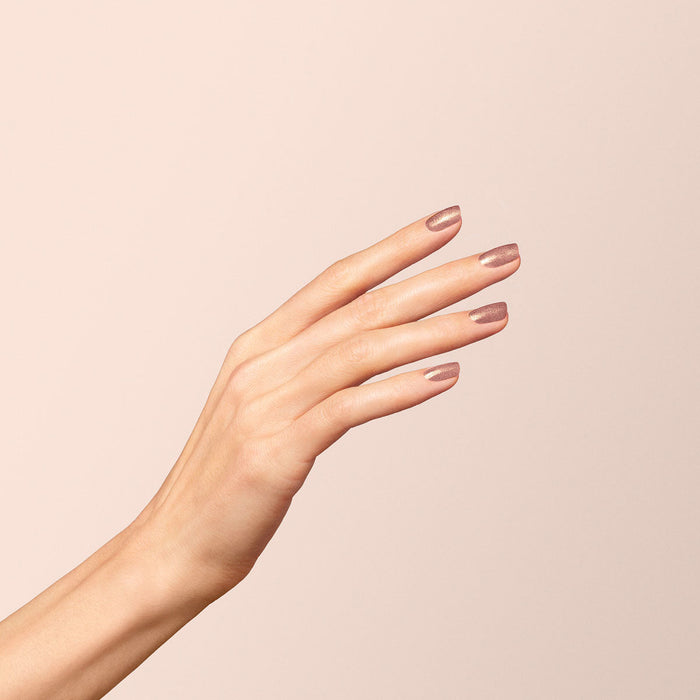 A close-up of a hand with slender fingers and neatly manicured nails painted in Manucurist's Cosmic Rose polish, held against a light beige background.