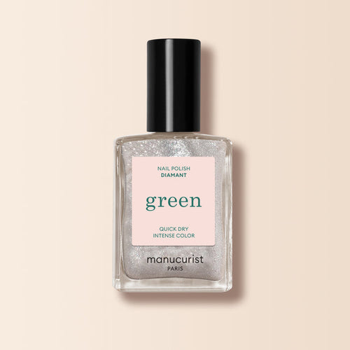 A bottle of Manucurist Diamant nail polish from the Green range, featuring a clear silver glitter shade, black cap, and pale pink label, displayed on a light beige background.