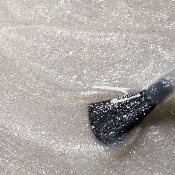 A close-up of Manucurist's Diamant brush applying shimmery silver nail polish, creating sparkling, textured streaks in a stunning silver shade.