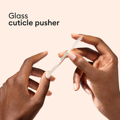 Two hands hold a glass cuticle pusher against a peach background. Text reads “Glass nail accessory trio” by Manucurist-us. The tool gently pushes back cuticles—ideal to pair with your favorite glass nail file for flawless nails.