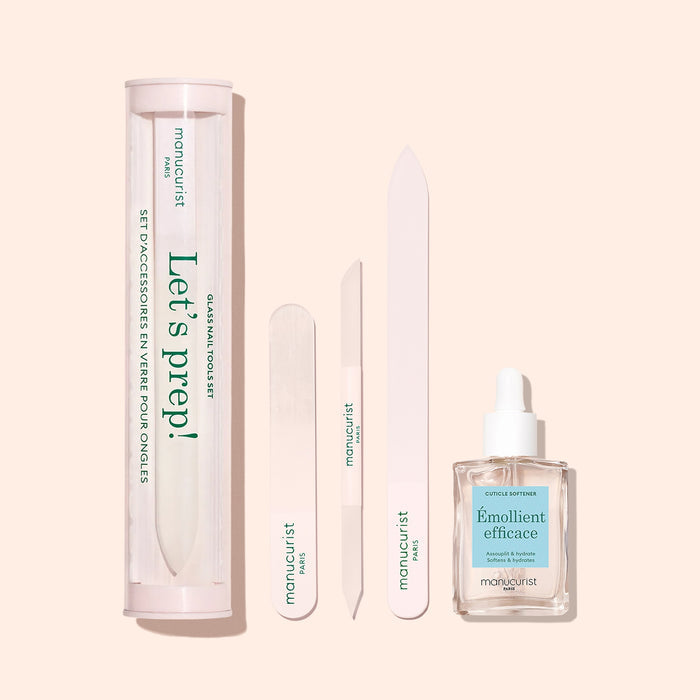 The Manucurist-us Glass nail accessory trio, including a glass nail file, buffer, and straight file, plus a cuticle pusher and softener in a square dropper bottle, is displayed on a beige background.