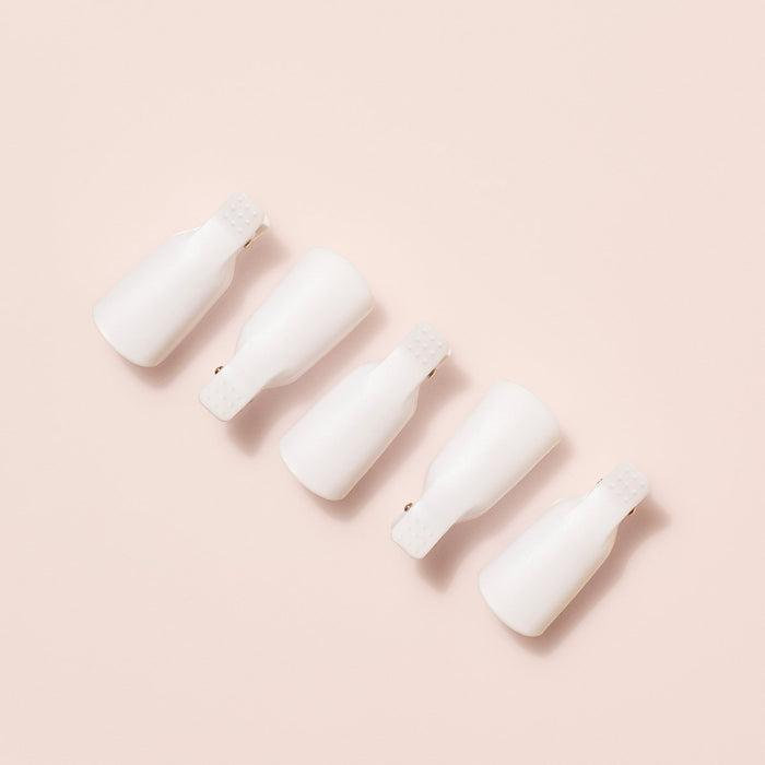 Five white plastic nail clips from Manucurist-us Green Flash™ Remover  Clips Duo are arranged in a neat diagonal line on a light beige background. Perfect for use with plant-based nail polish remover.