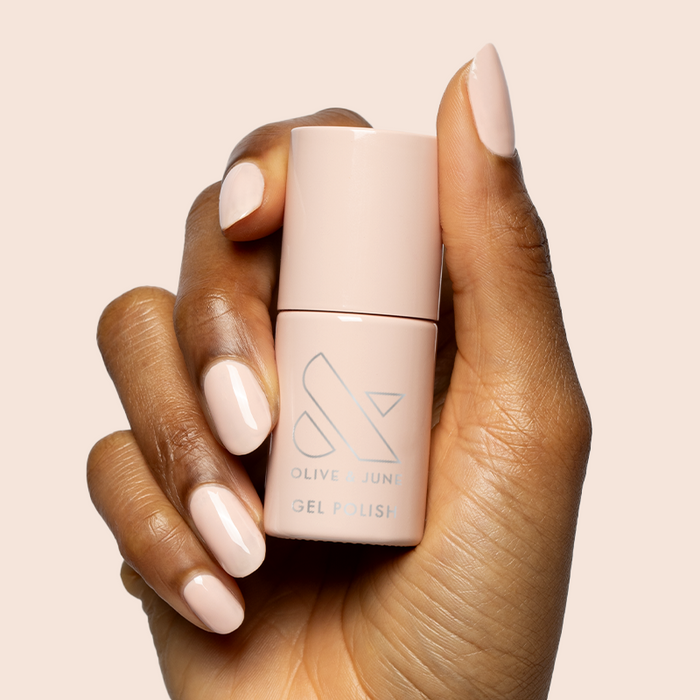 Hand with nails painted in KAG - Gel neutral peachy pink polish holding matching bottle on soft beige background