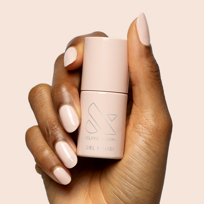 Hand with nails painted in KAG - Gel neutral peachy pink polish holding matching bottle on soft beige background