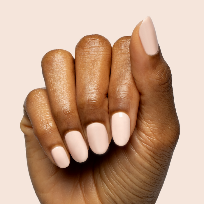 Hand with nails shaped and painted in KAG - Gel neutral peachy pink gel polish on smooth warm beige background