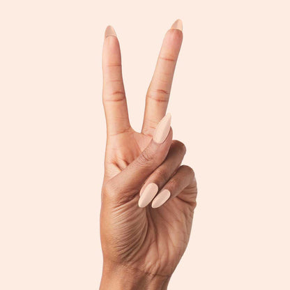 KAG - Press-On | Long | Almond showing hand with long almond press-on nails in neutral peachy pink polish on light background