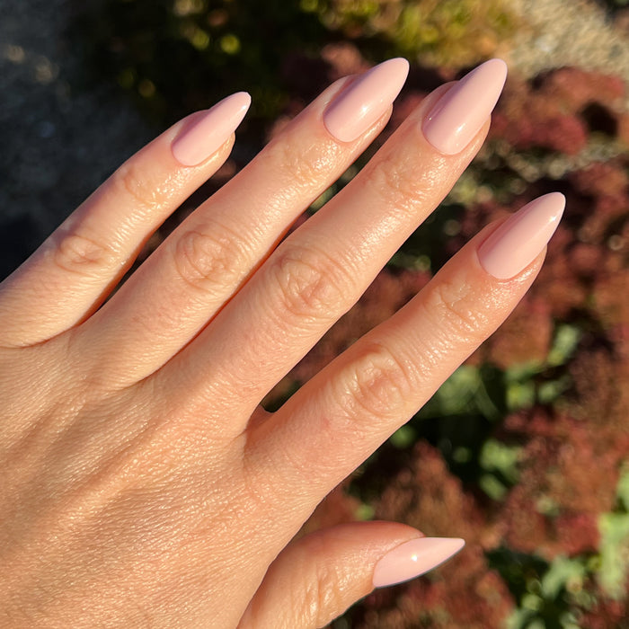 KAG - Press-On | Long | Almond showing hand with long almond press-on nails in neutral peachy pink polish outdoors