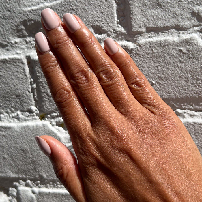 Kitten | Extra Short | Round - Tab Press-On showing soft neutral pale pink press-on nails on hand against white brick wall background