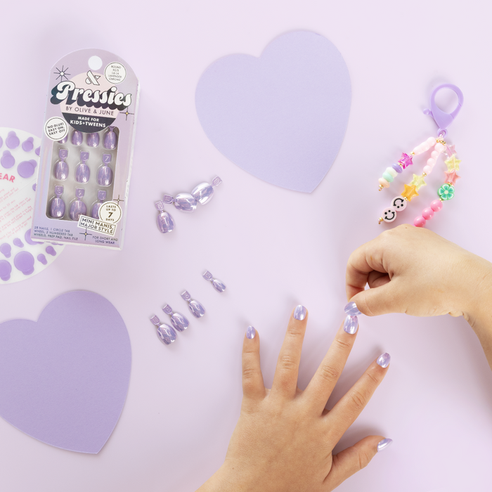 La La Lavender Chrome - Pressies | Extra Short Short | Round showing hand with lavender chrome press on mani and playful kid accessories on purple background