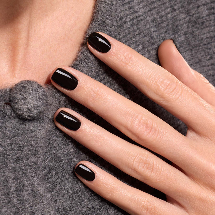 A close-up of a hand with neatly manicured nails painted in Licorice by Manucurist, resting on soft, textured gray fabric.