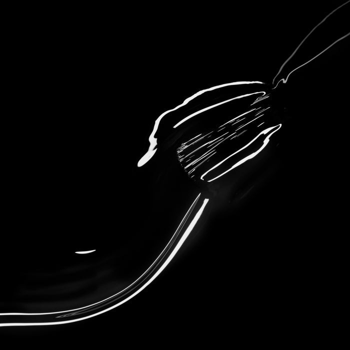 The Manucurist Licorice metallic fork reflects light on a chic black background, creating abstract bright lines and highlights.