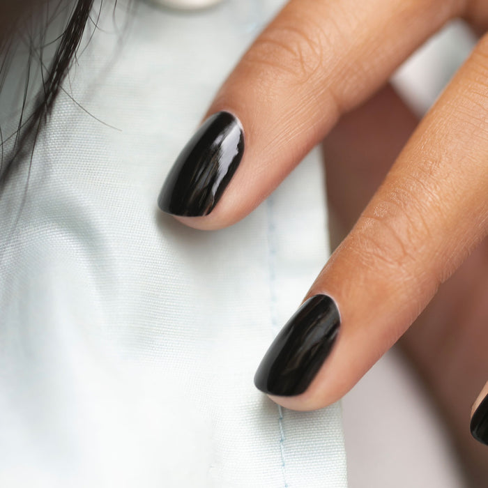 Close-up of two fingers with well-groomed nails painted in Licorice, a chic black nail polish from Manucurist, resting on light blue fabric.