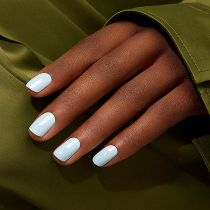 A hand with medium brown skin and neatly manicured nails painted in Manucurist Light Blue nail polish rests on olive green fabric.