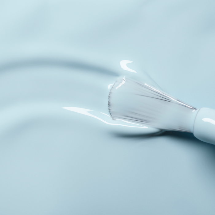 A close-up of a Manucurist brush applying Light Blue nail polish to a smooth surface.