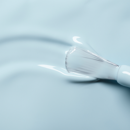 A close-up of a Manucurist brush applying Light Blue nail polish to a smooth surface.