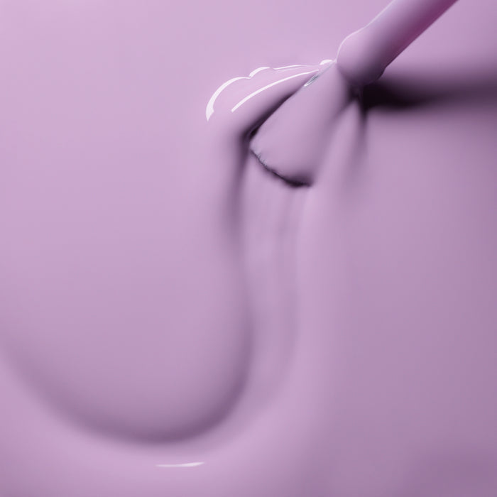 A close-up of a brush applying smooth, glossy Lisa Lilas nail polish from Manucurist in sweeping strokes on a flat surface.