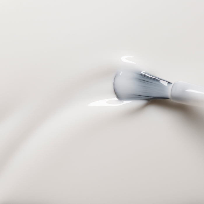 A close-up shows a Manucurist brush gently applying Milky White gel polish onto a smooth surface, with the soft, glossy formula spreading evenly as the bristles fan out slightly.