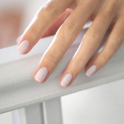 A close-up of a hand with neatly manicured nails painted in Manucurist’s Milky White, a soft, sheer gel polish, resting gently on a white surface.