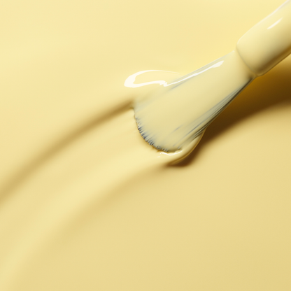 A close-up of a brush applying smooth, pastel yellow Mimosa nail polish from Manucurist in even strokes on a matching yellow surface.