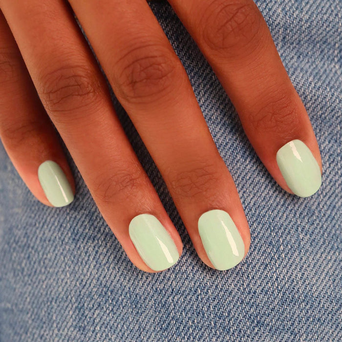 A hand with neatly manicured nails painted in Mint, a glossy pastel green nail polish from Manucurist, rests on blue denim fabric.