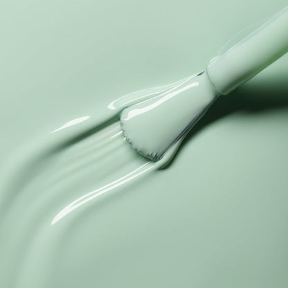 A close-up shows a brush spreading Manucurist's Mint nail polish over a smooth surface, with the bristles and handle partially visible against the creamy pastel green texture.